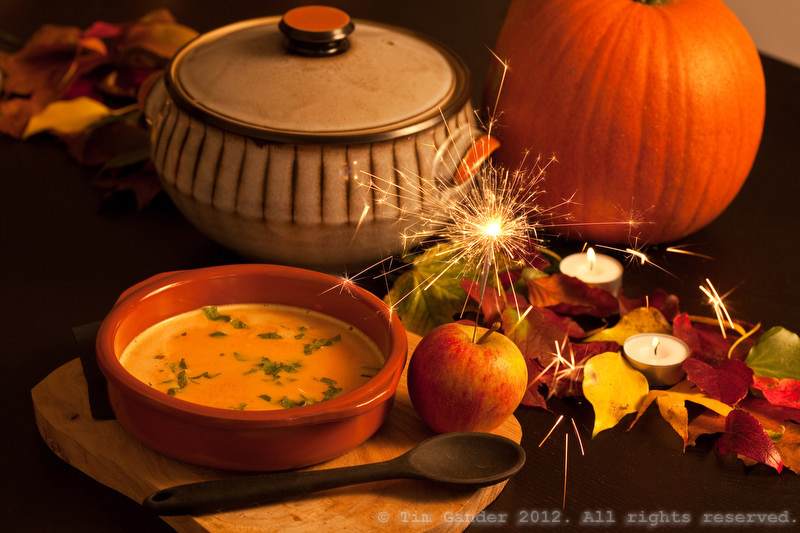 Pumpkin soup in a bowl, with sparkler lit in an apple