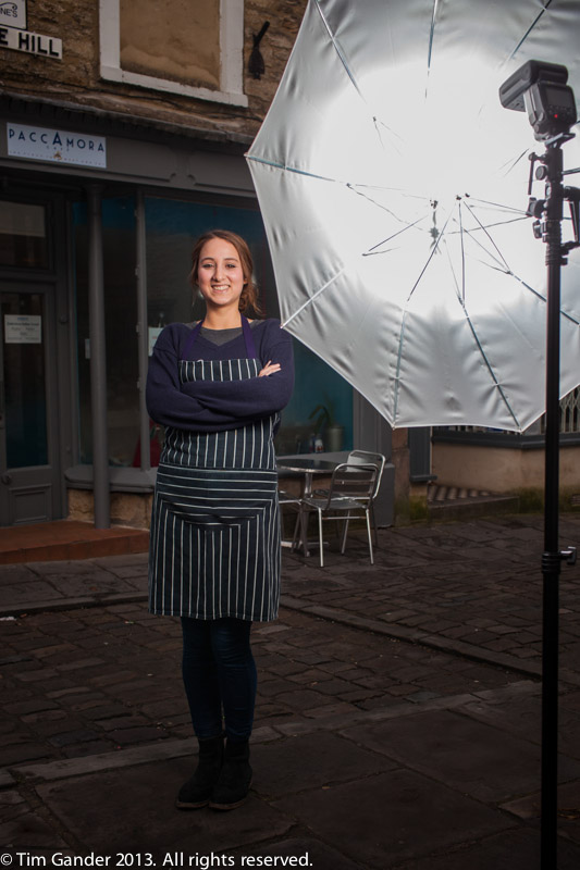 Waitress poses in the street in front of a photo flash on a stand with a white brolly