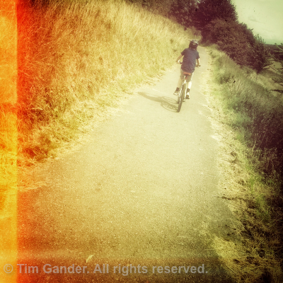 Hipster photo of boy on a bicycle on a cycle path, filtered with muted colours and orange light leaks