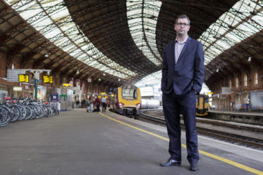 Profile photo of Dan Panes of First Great Western stands on Platform 1 at Bristol Temple Meads station with the station canopy, engine and passengers visible in the background.