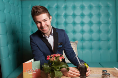 Portrait of Josh Gottschling of Jolly's, Bath, seated at a table with a cocktail in his favourite bar in Bath.