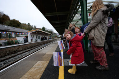 Little girl on red dress waves a Dartmoor Line flag as she waits for the first passenger train in 49 years.