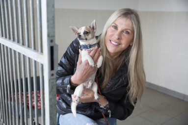 Olympic swimmer Sharron Davies holds a small dog in her hands and smiles to camera.