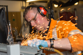 Tim Laws Chapman of Arriva grinds a metal section he's just welded. He's wearing eye and ear protection as well as gloves as sparks fly.