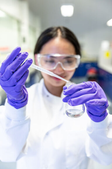 A young female student in a chemistry lab pipettes liquid into a jar.