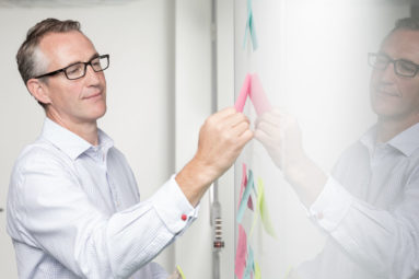 A business man places sticky notes on a gloss wall which reflects him.