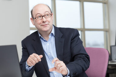 A male colleague at eduserv in bath talks to someone off-camera while seated at his desk.