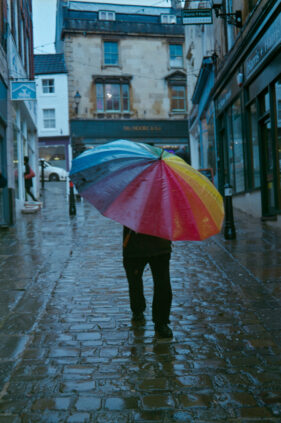 A man battles with a multi-coloured umbrella as he walks down a cobbled street in Frome, Somerset.