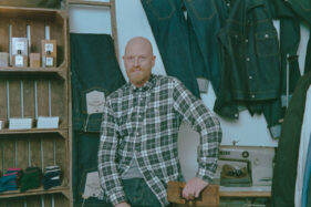 Anthony Hick of Assembly Shop poses in his Catherine Hill store with jeans and an old industrial sewing machine around him.