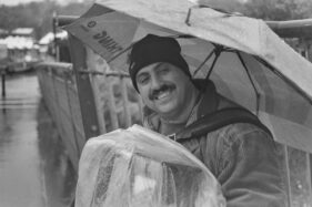 An accordion player on the bridge to the Cheese and Grain market keeps himself and his instrument dry with a brolley and plastic cover.