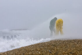 Two men brave the wind, waves and flying pebbles on Hayling Beach.