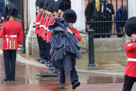 ONE GUARD IS WEIGHED DOWN BY HIS COLLEAGUES'S RAIN CLOAKS, WHICH HE HAS TO COLLECT BEFORE THE ROYAL PROCESSION PASSES. PHOTO/TIM GANDER