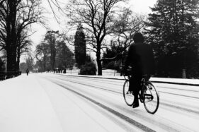 Victoria Park in Bath under snow, circa 1988. A cyclist in black rides in from the right of the image as the road leads into the distance.