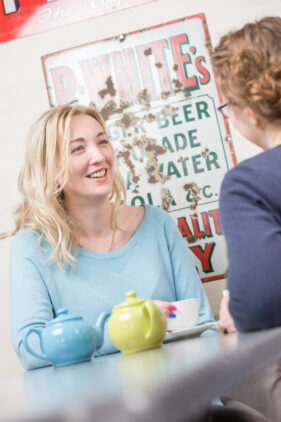 Debbie Clifford of Tea for Three sits chatting to a friend in a cafe over cups of tea.