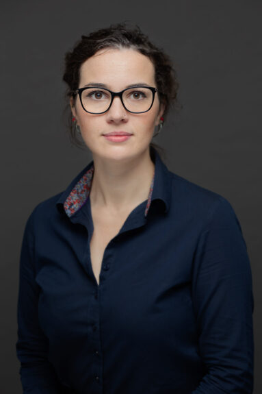 Low-key portrait of a young female architectural assistant wearing glasses, looking directly into camera, not smile.