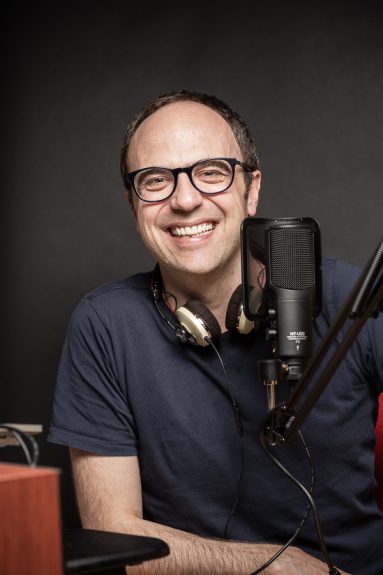 17 May 2018 Head of Class:PR Alistair Clay smiles to camera with headphones around his neck and a podcast microphone to his side.