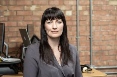 17 May 2018 Head-shot of Gemma Keogh Class:PR in their office with computers, a brick wall and pipes behind.