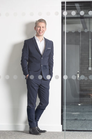 Full-length profile photo of a business man seen through the glass wall of a corridor.