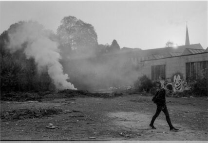 A fire burns on the open Saxonvale site as a young man strides away, looking at his mobile phone