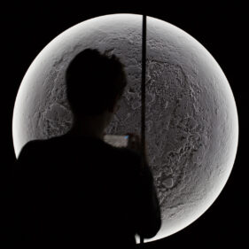 A detail from Illuminator XVII, a modern art installation which resembles the surface of the moon. A silhouetted figure of a lady taking a photo partially obscures the view of the piece.