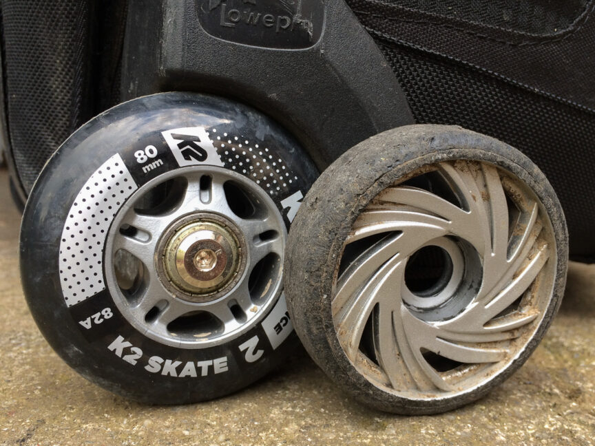 New inline skate wheel fitted to a rolling camera bag with the old wheel standing adjacent for comparison.