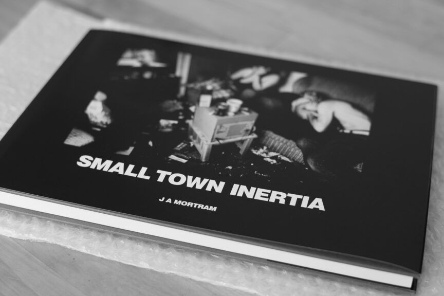 A black and white photo of a copy of Small Town Inertia by J.A Mortam rests on the bubblewrap it arrived in on a coffee table.