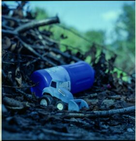 A colour photo of a blue plastic toy tractor and a blue bleach bottle on a pile of twigs.