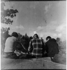 Three young men sit on a concrete platform, their backs to the camera.