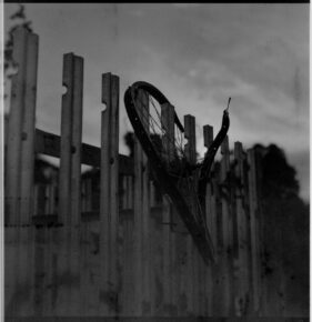 A smashed bicycle wheel hangs on a metal fence.