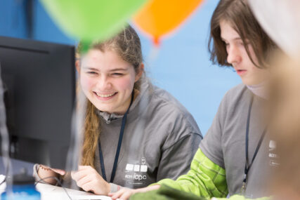 A German student smiles as she and her male colleague work at their computer screen.