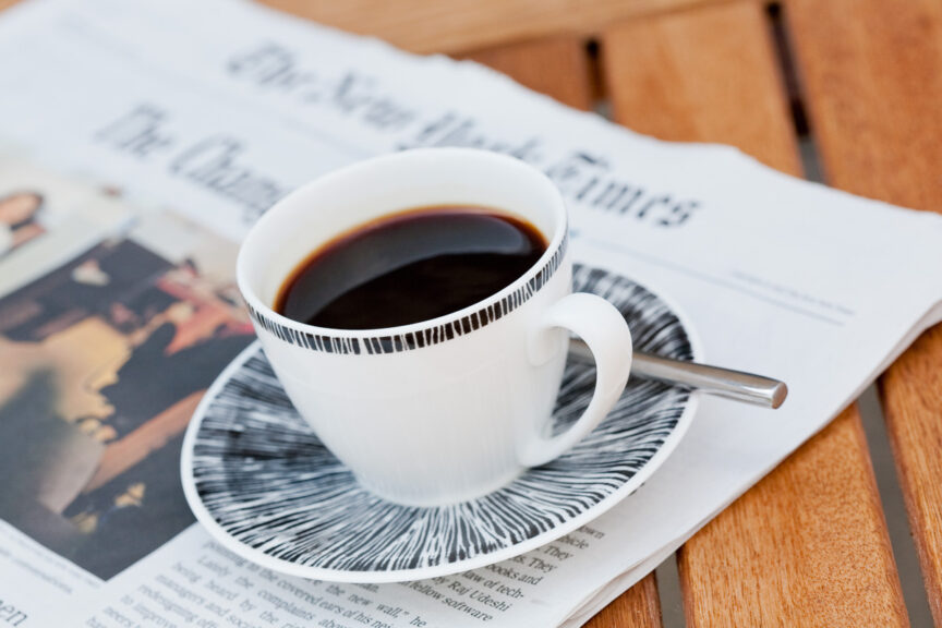 A cup of espresso sits on an out of focus copy of the New York Times.