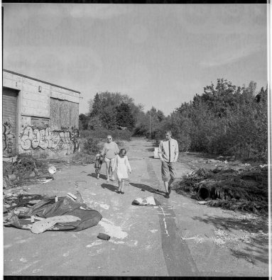 Black and white photo of a family of mum, dad, daughter and son walking through the littered site.