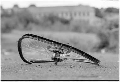 Black and white ground-level view of a badly mangled bicycle wheel with no tyre.