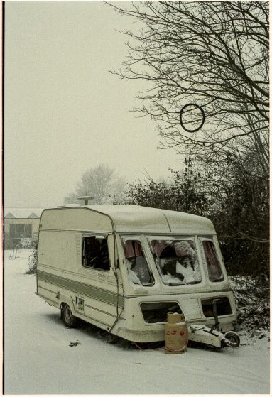 Colour photo of Alby's caravan, vandalised. There is snow on the ground and a bicycle tyre hangs in a tree above the van.