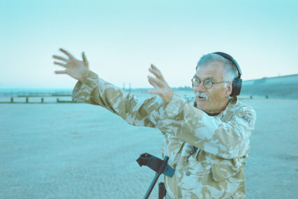 A detectorist on the beach looks off-camera to the left and gesticulates as he tells a story.