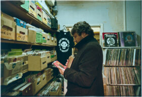 A male customer in a black coat looks through boxes of vinyl 45rpm records.