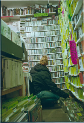 Floor-level view of a female customer, kneeling and looking up at racks of CDs.