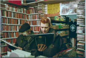 A woman with red hair looks intently at the back of a record sleeve while another woman to her side looks at another.