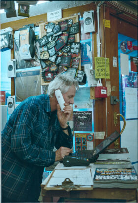 Shop owner Richard Churchyard holds a phone to his ear as he looks down at a laptop.