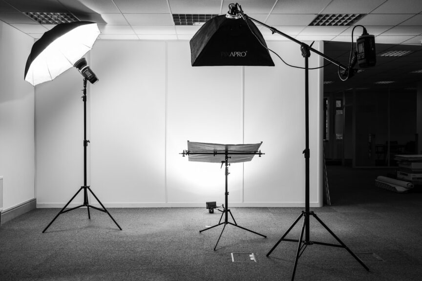 Photo shows a portable photographic studio lighting set up with three flash heads and a reflector in an empty office space.