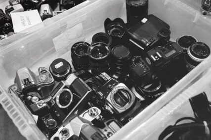 A plastic crate full of old camera bodies and lenses.