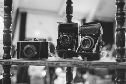 Three early film cameras on a wooden display shelf.