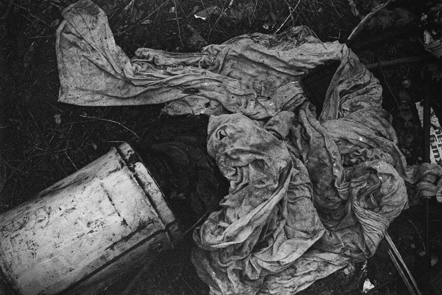 Black and white view of an upturned large metal can with dirty rags strewn nearby.