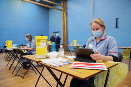 Clinical nurses at tables in a school gymnasium with blue walls prepare to vaccinate school pupils in Trowbridge.