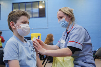 A school pupil in his school sports hall is vaccinated by a nurse.