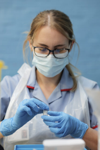 A nurse in mask and apron dilutes a vial of Pfizer vaccine by turning it in her fingers 10 times.