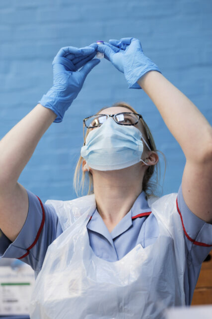 A registered nurse holds up a vial of vaccine to the light to check it is still clear and good to use.