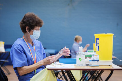 Nurses at tables in a school sports hall prepare syringes with vaccine prior to administering the injections.