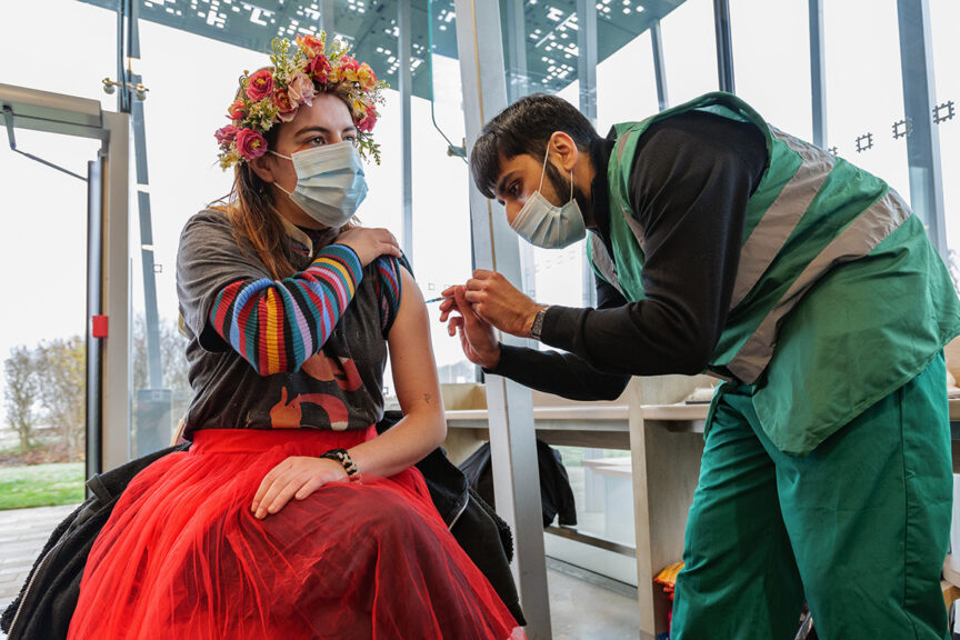 A young woman in colourful Winter Solstice costume is vaccinated by a man.