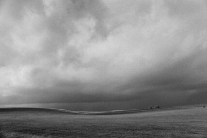 Square black and white minimalist landscape photograph taken near Chitterne, Wiltshire, with dark clouds above an undulating grass landscape